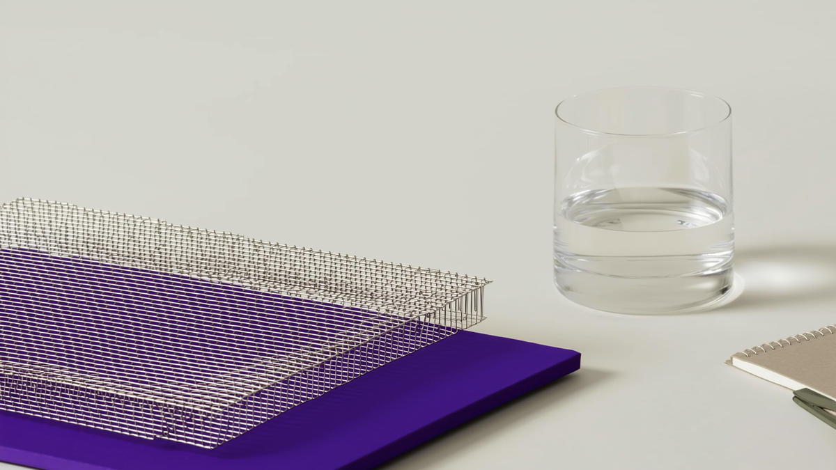 A woven stainless steel mesh panel on a purple surface beside a glass of water and a notebook.